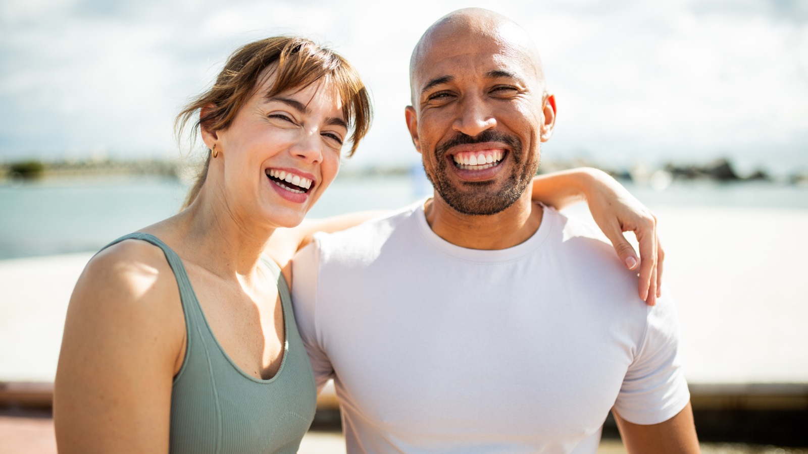 Two people laughing together outdoors by the water.